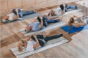 senior people with instructor stretching and exercising on yoga mats at training class